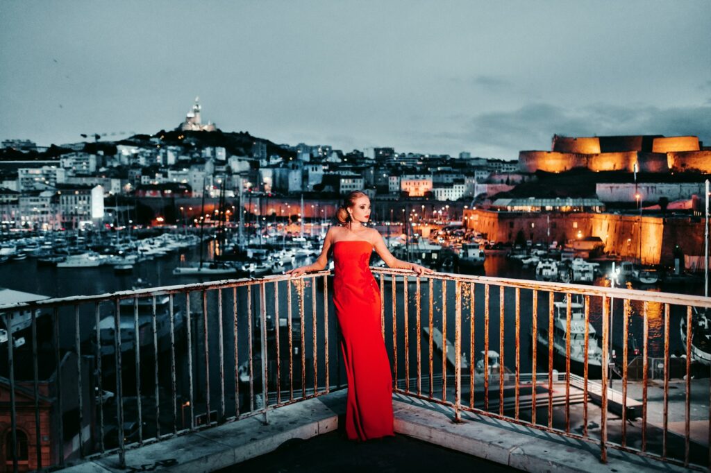 Une fille élégante vêtue d'une robe de soirée rouge dans les rues de la ville nocturne de Marseille.